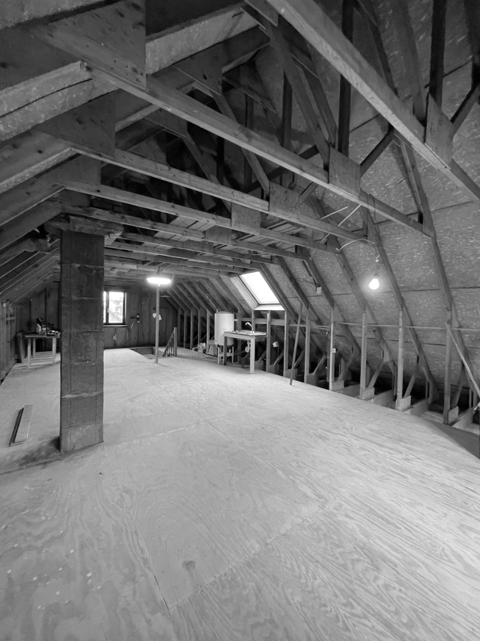 Onvoltooide zolderruimte onder constructie met houten frame, werkbank en verlichtingspunten.