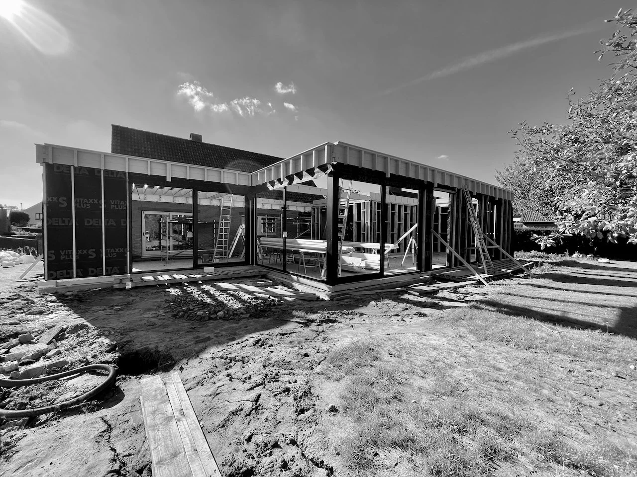 Bouw van een nieuwe woning in aanbouw met houten structuur, ladders en bouwmaterialen op de bouwplaats.