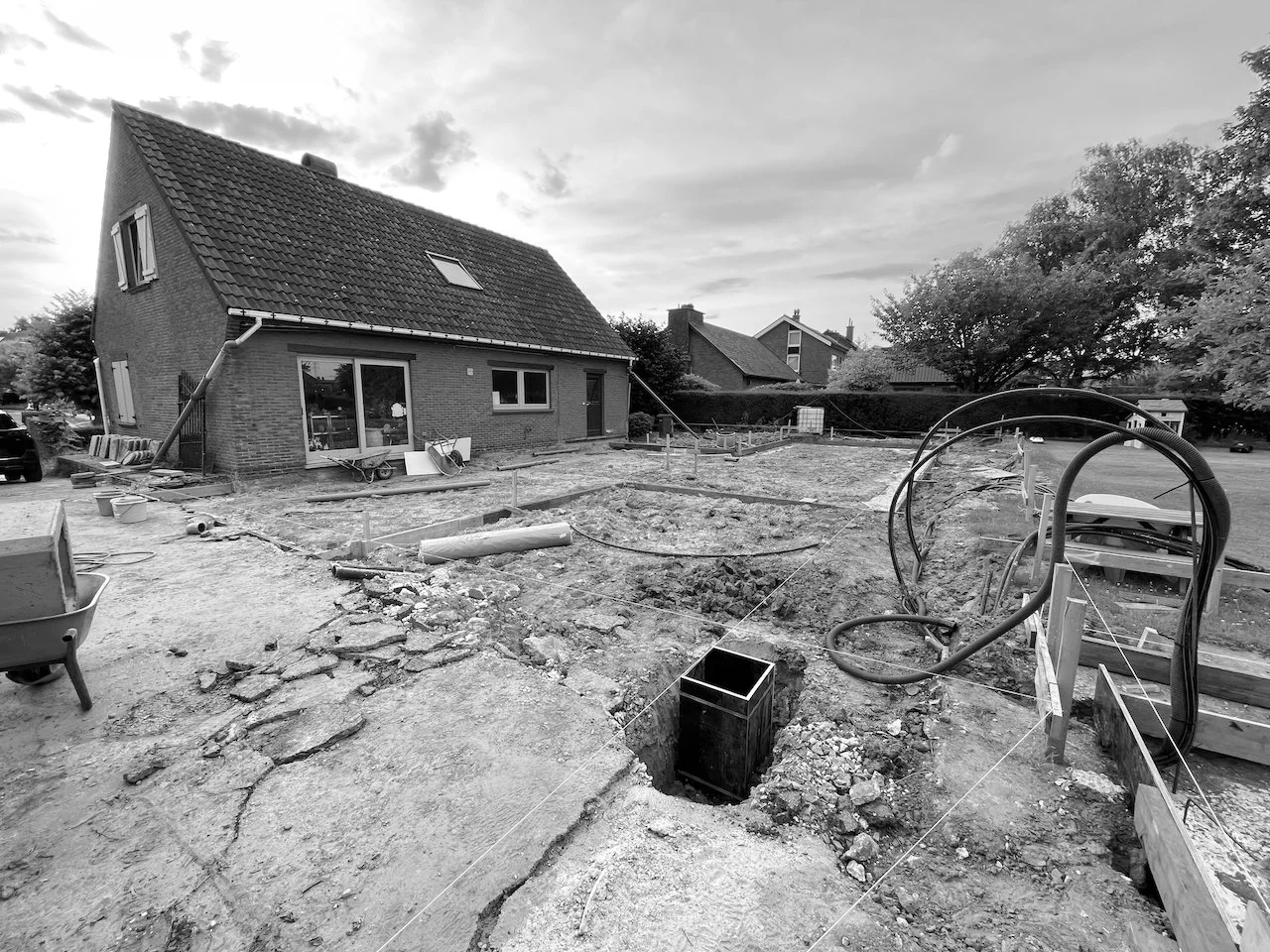 Een huis onder constructie, met graafwerk en bouwmaterialen op een bouwterrein.