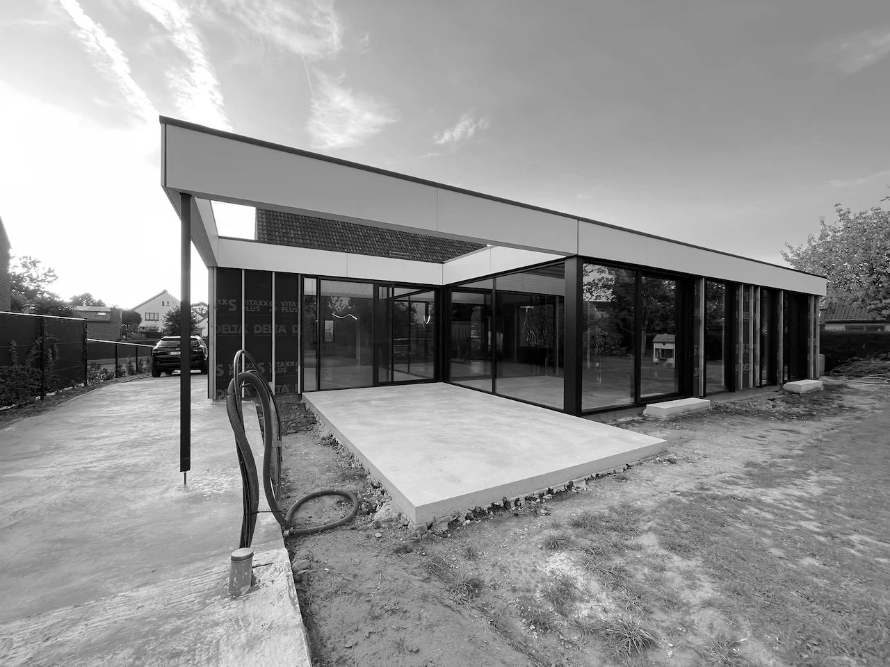 Moderne eengezinswoning met grote glasramen en een vlakke, licht hellende dakrand in een nieuwbouwgebied, uitzicht in zwart-wit.