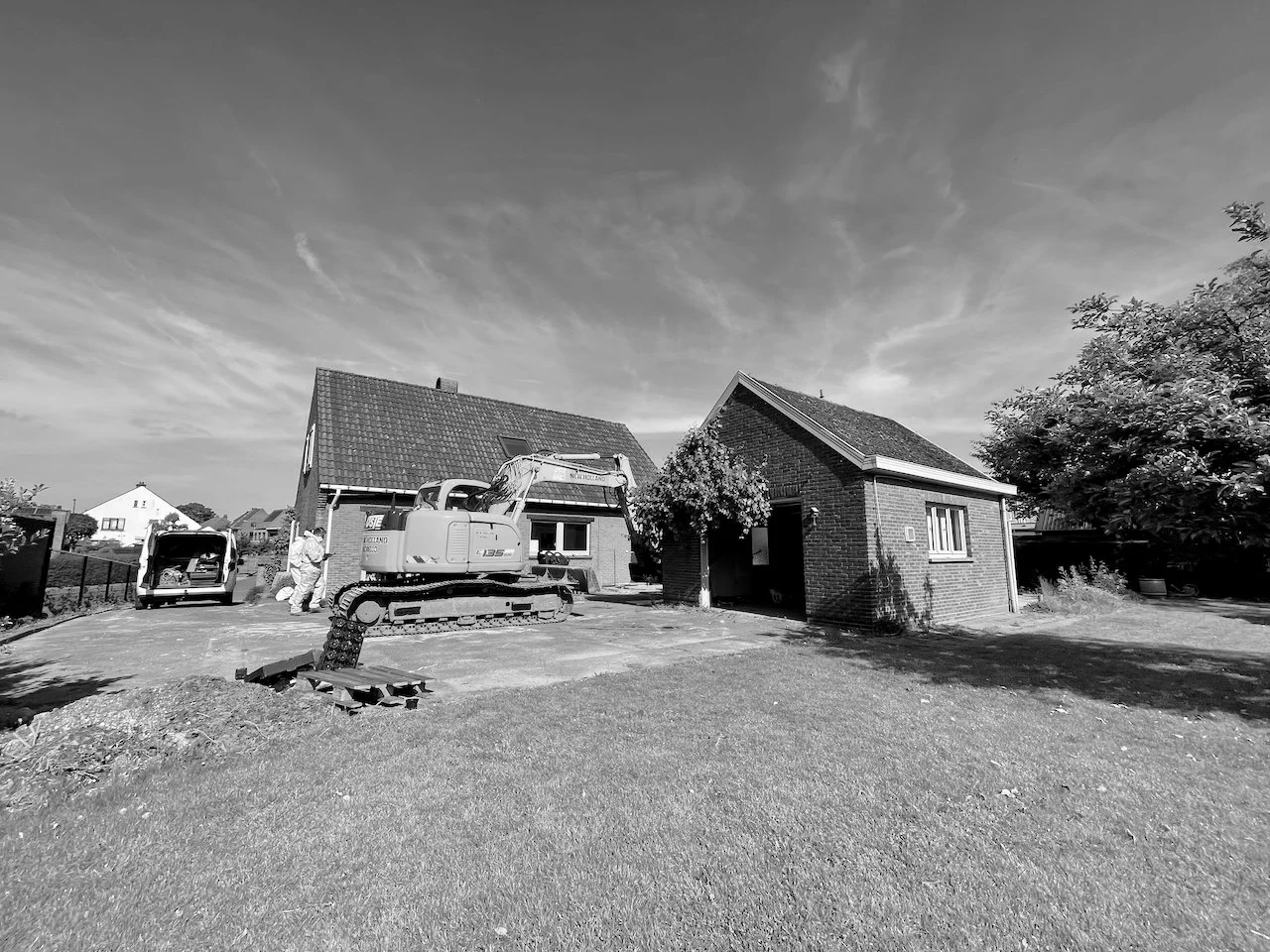 Twee huizen in uitbouw, met bouwmachines en bouwvakkers die werken, in een tuin met gras en bomen.