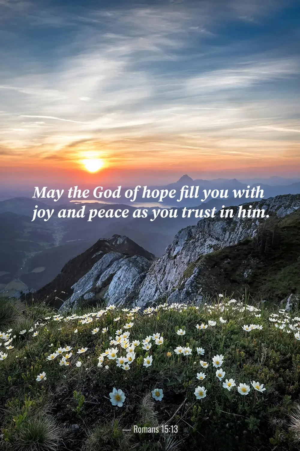 Romans 15:13 Bible verse over a mountain sunrise with wildflowers, celebrating hope, joy and peace through faith.