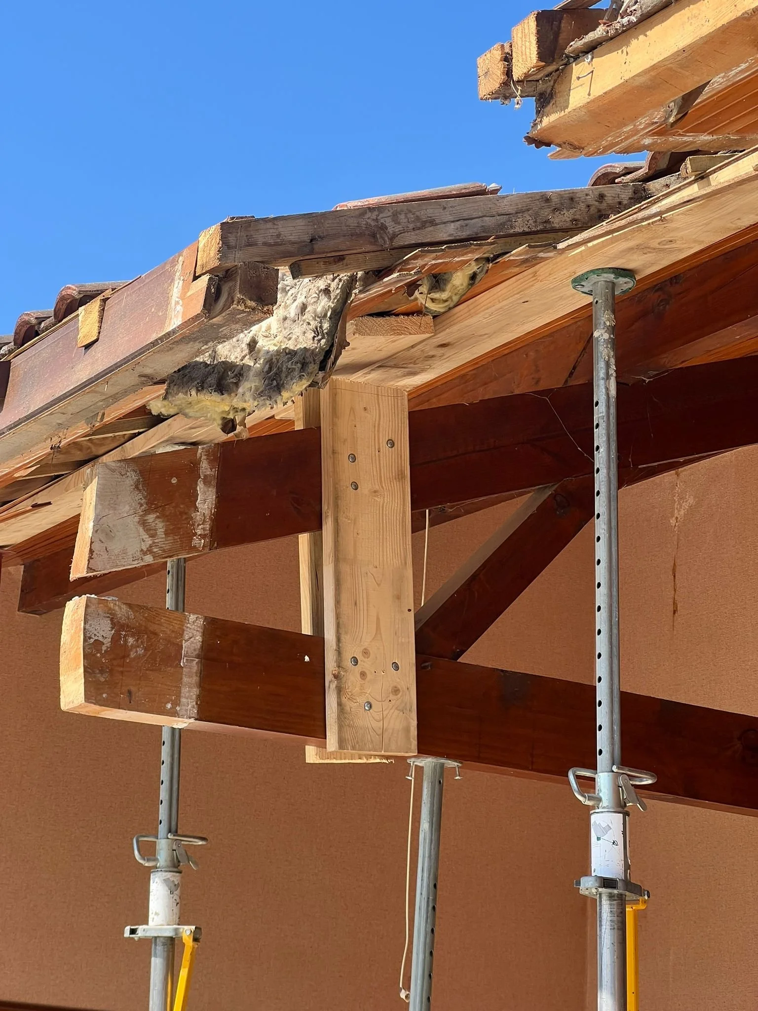 Travaux de rénovation du toit d'une maison avec des supports métalliques et bois, des matériaux isolants visibles, et un ciel bleu en fond.