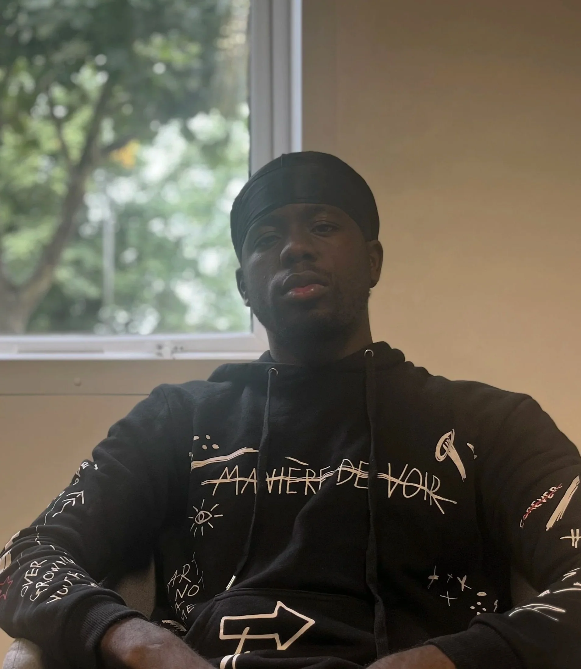 A man sitting in a recording studio at a desk with audio equipment, including speakers, a mixer, and a laptop, smiling at the camera.