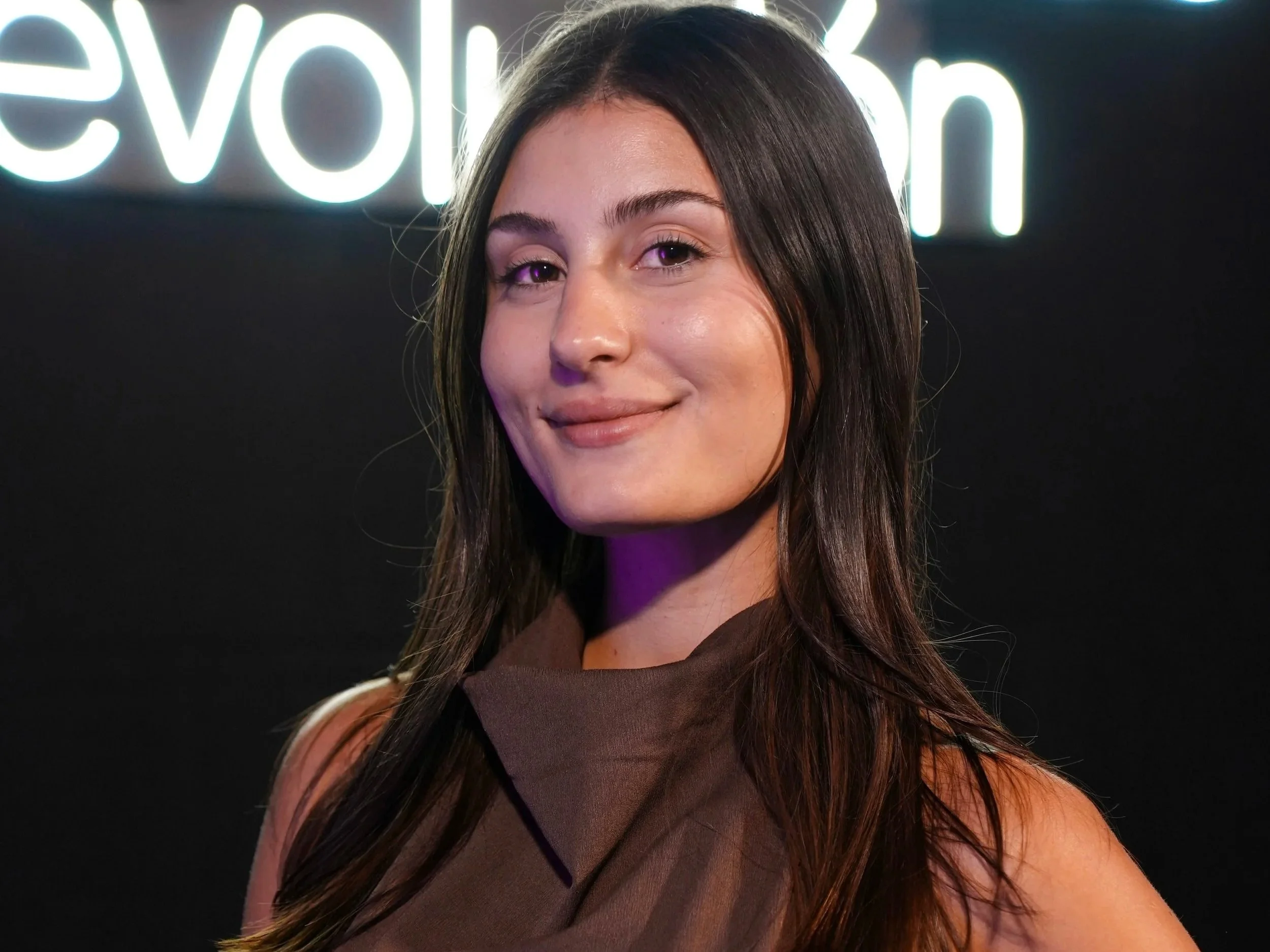 Mujer sonriendo con fondo de neón que dice 'revolución'.