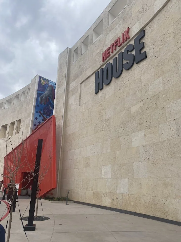 Exterior view of the Netflix House building with large black and red signs, part of a mural visible at the top left, and a red structure at the entrance.