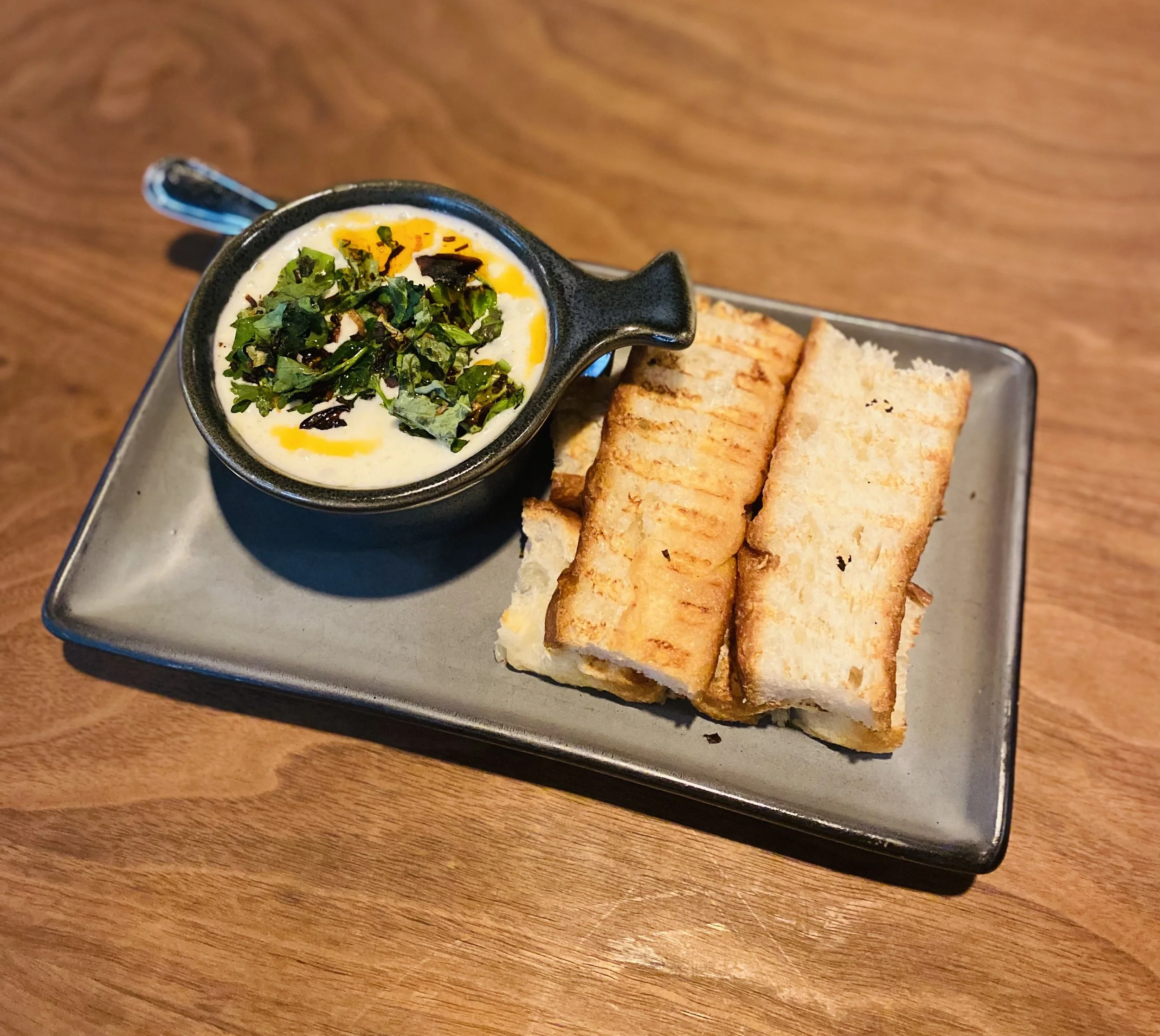 Grilled sandwiches with a side of fried eggs topped with herbs on a black rectangular tray.