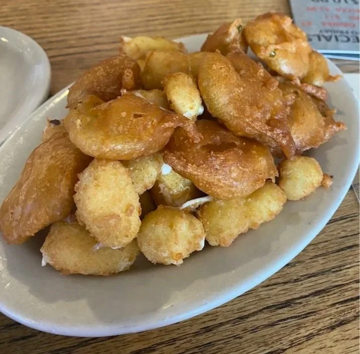 A white oval plate filled with battered and fried fish pieces on a wooden table.