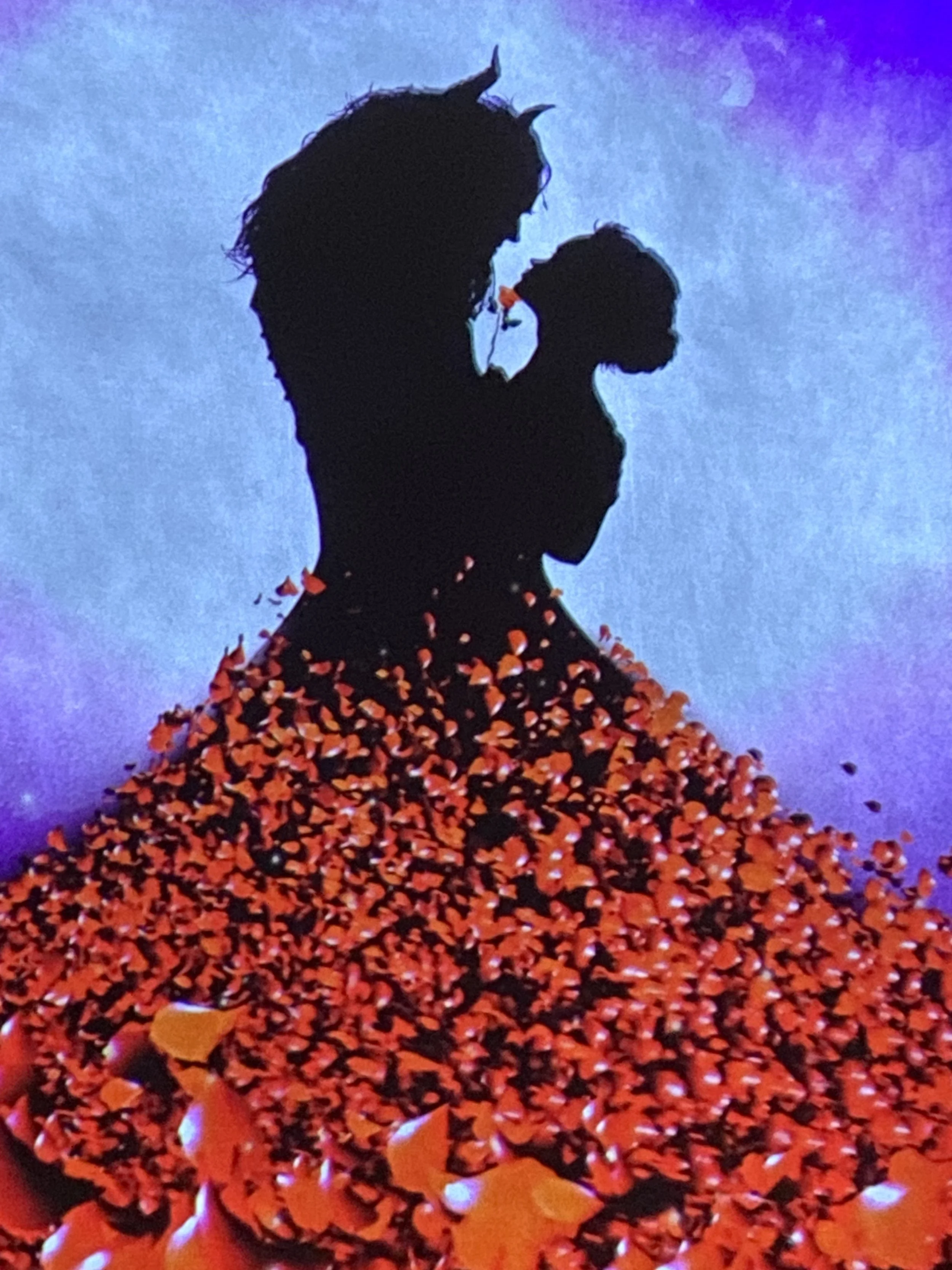 Silhouette of a woman holding a child, with red flower petals or confetti falling around them, against a colorful purple and blue background.