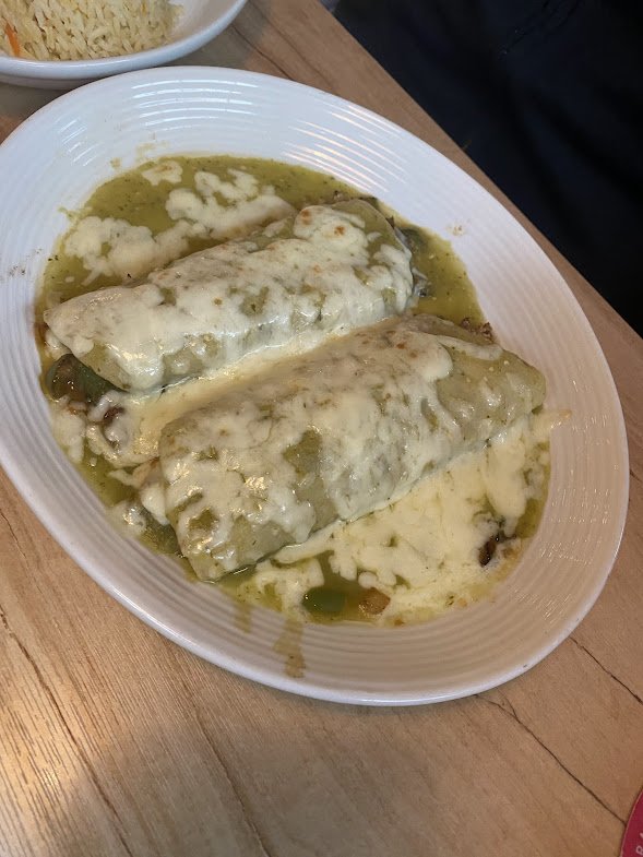 Two stuffed green peppers covered in melted cheese and sauce on a white oval plate.