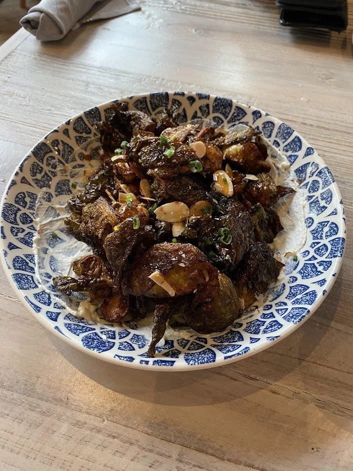 A bowl of roasted or braised chicken wings garnished with chopped green onions and sliced garlic on a decorative blue and white plate.