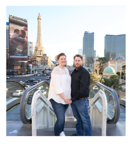 A smiling couple stands on an escalator with the Eiffel Tower replica and Las Vegas skyline in the background.