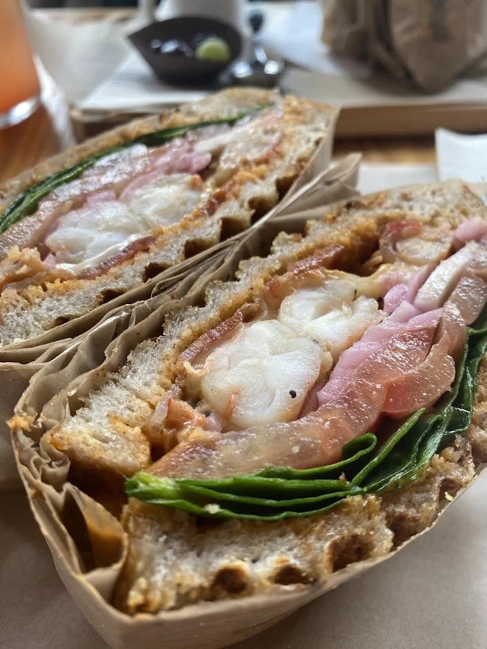 Two half sandwiches with shrimp, ham, green onions, cheese, and bread in a restaurant setting.