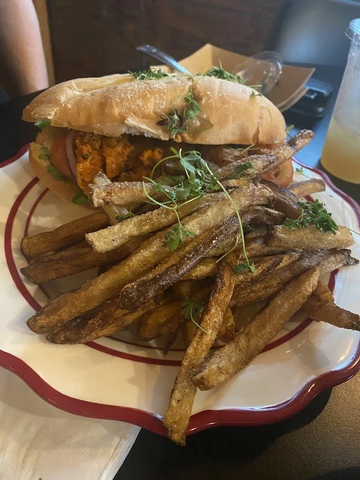 A plate of French fries topped with microgreens with a sandwich and a drink in the background.