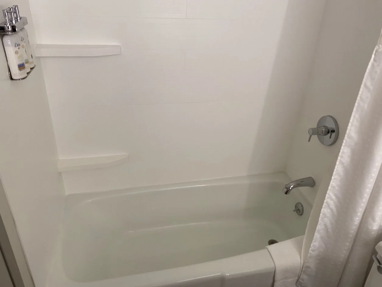 A plain white bathtub with a wall-mounted faucet, a shower head, and two small built-in shelves in a bathroom.