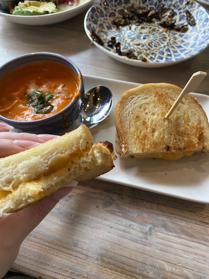 A plate with a grilled cheese sandwich, a bowl of tomato soup, and a small plate of salad in the background.