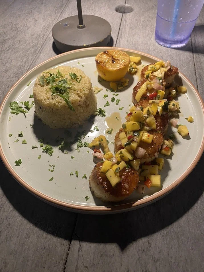 Plate with rice, a lemon half, and three pieces of fish topped with diced vegetables and herbs.