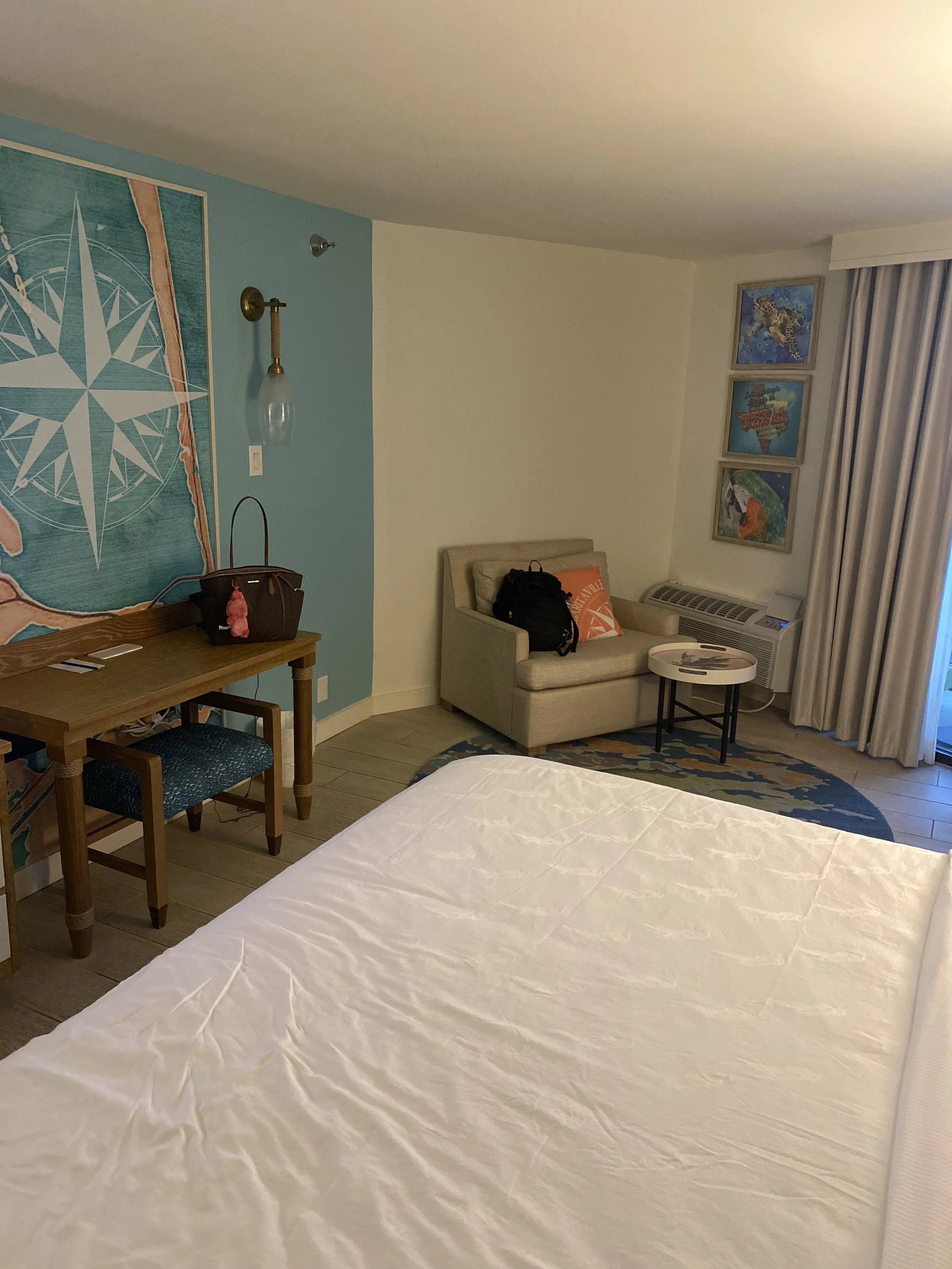 Hotel room with a bed, a small sofa, a round coffee table, wall art, and curtains.