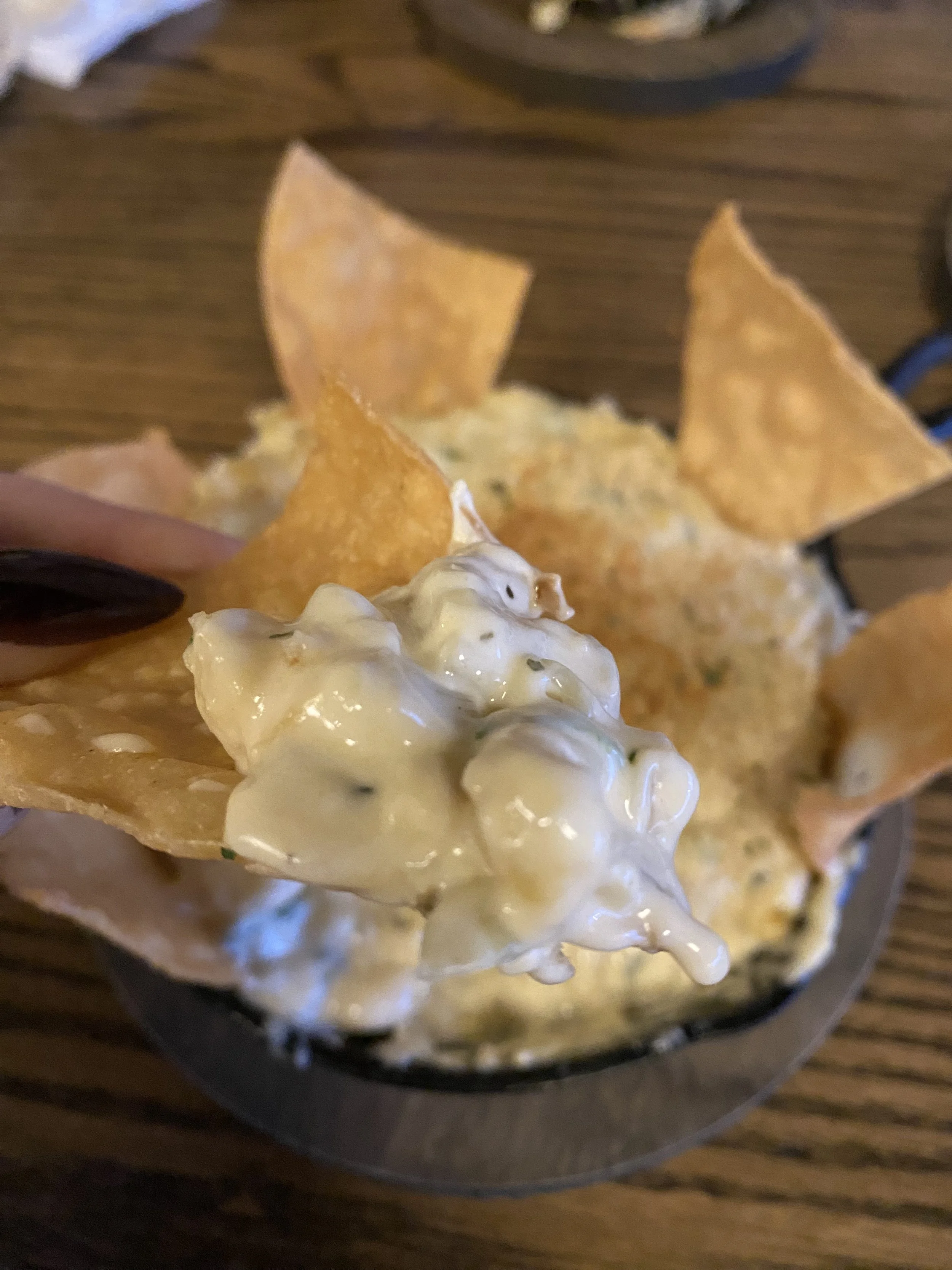 Close-up of a bowl of French onion dip topped with potato chips on a wooden table.