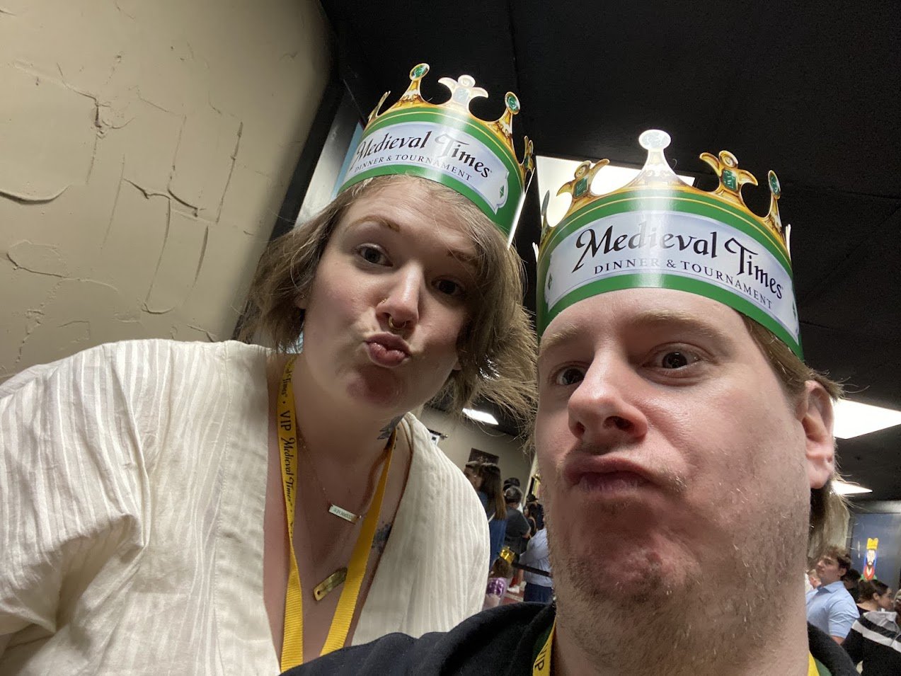Two people wearing medieval times crowns taking a selfie at a medieval-themed dinner event.