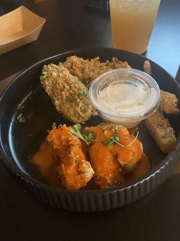 Fried chicken wings with orange sauce, served with a side of fried fish fillets, a container of dipping sauce, and a drink in a plastic cup.