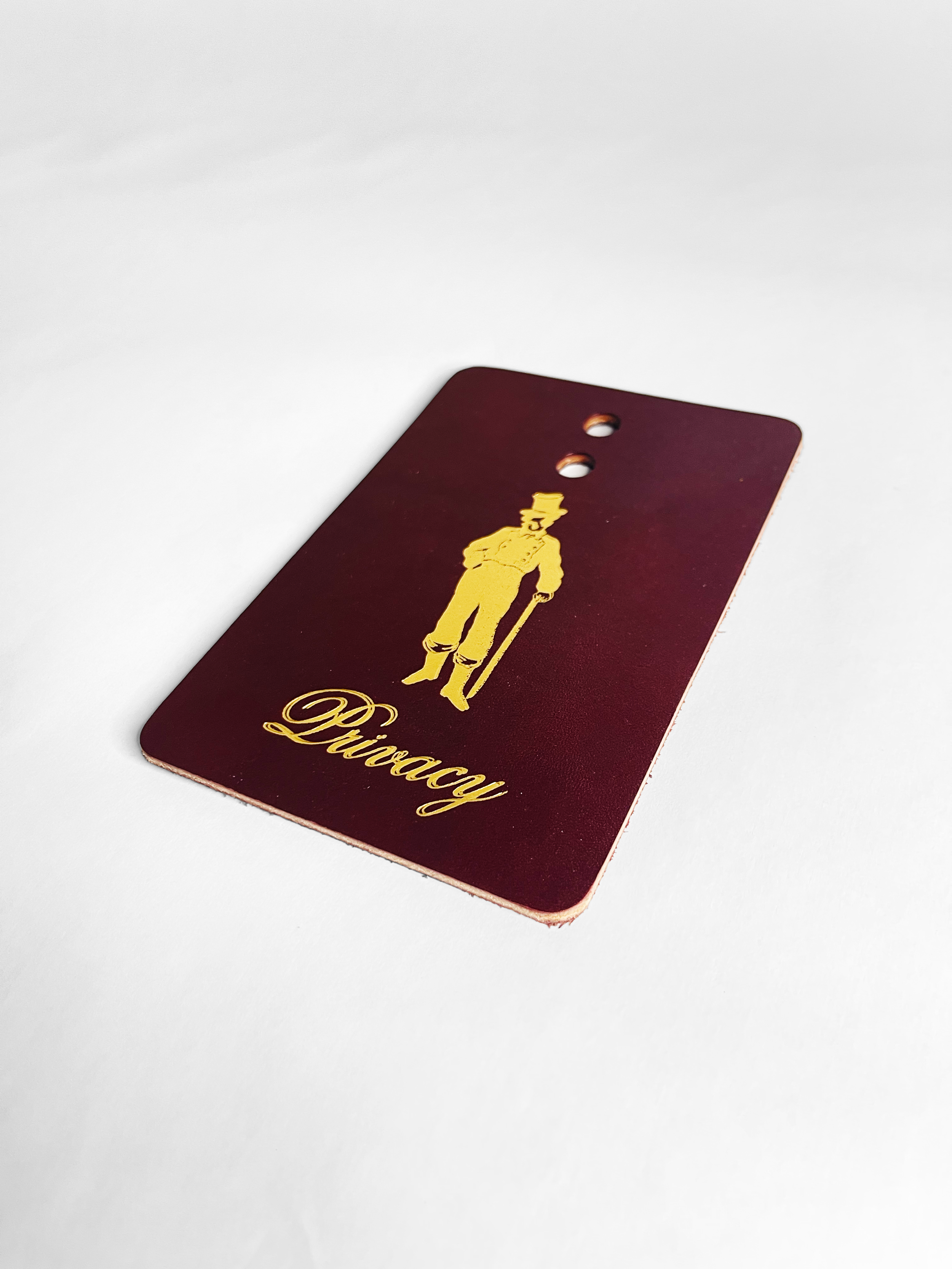 A burgundy-colored card with a golden illustration of a man in old-fashioned attire and the word 'Privacy' written in cursive.