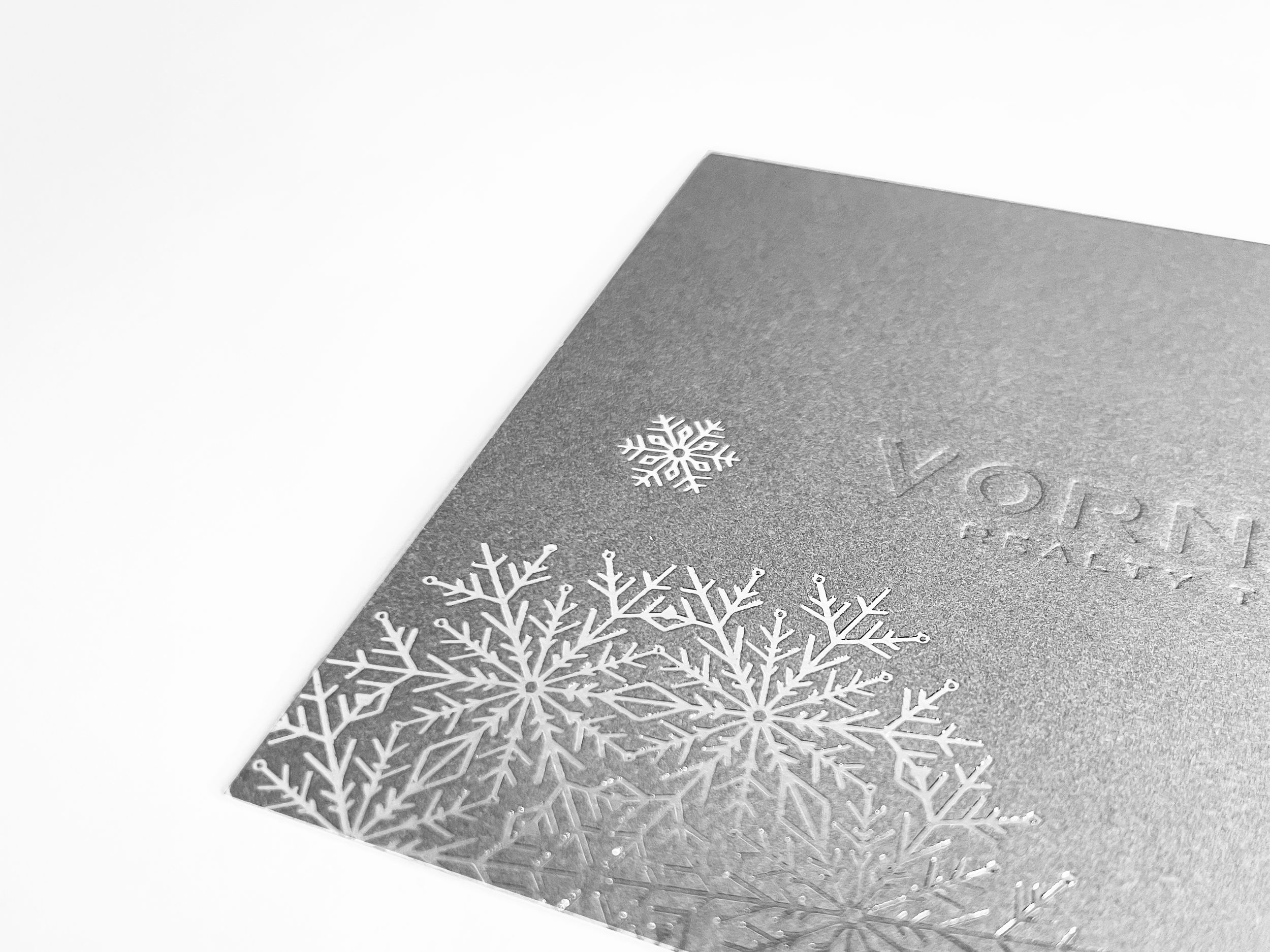 Silver holiday greeting card with embossed snowflakes and partial embossed text.