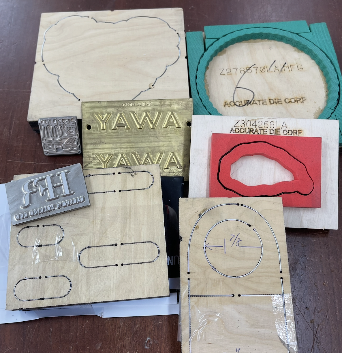Various metal stamps, cutouts, and templates used for metalworking or jewelry making, including letter stamps, outline templates, and patterned dies placed on wooden boards.