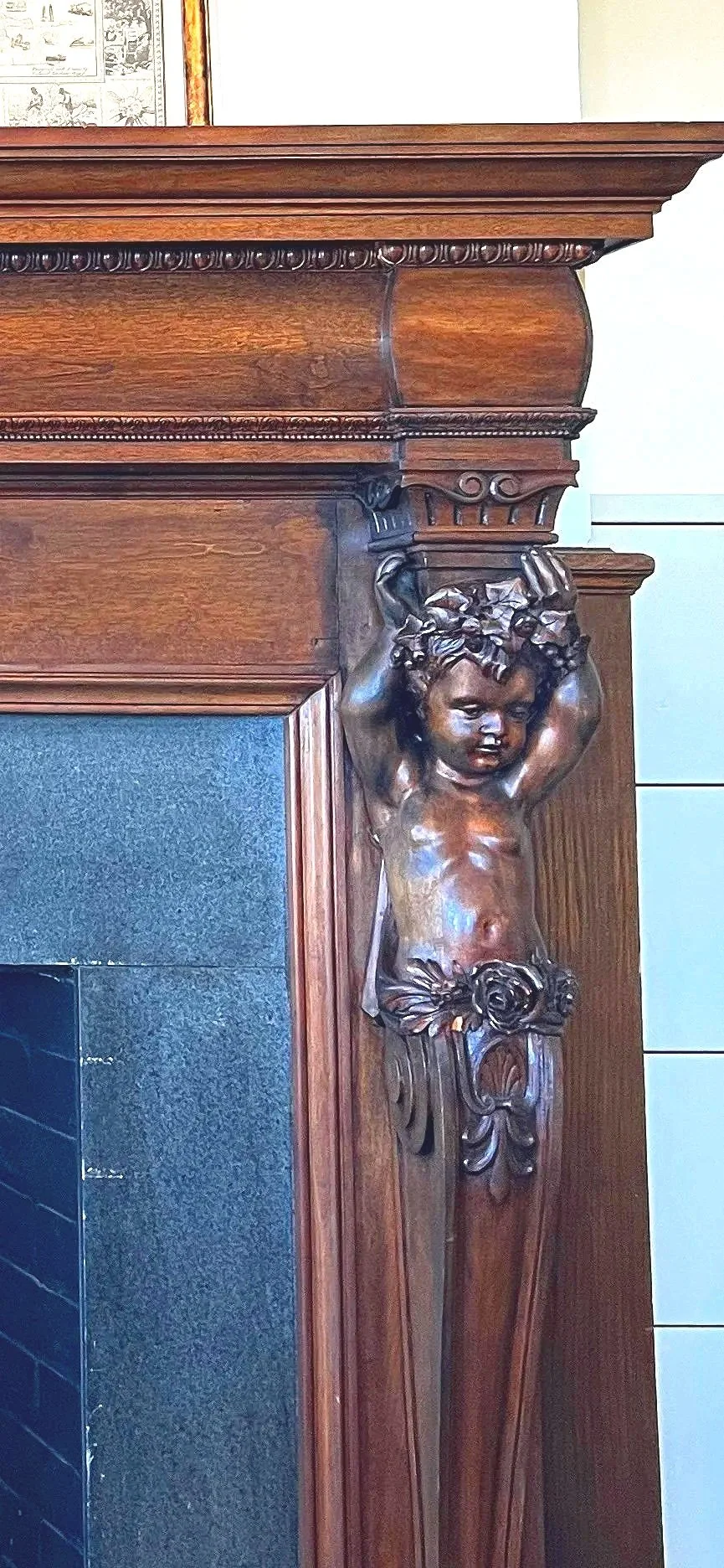 Close-up of a decorative wooden fireplace mantel with a carved cherub figure supporting the top of the mantle.