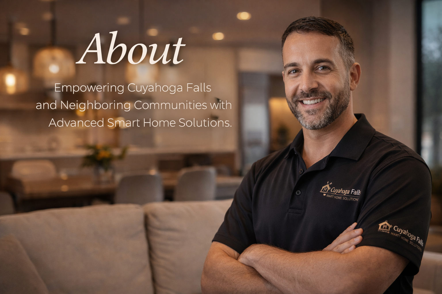A smiling man in a black polo shirt with a logo, standing in a modern, warmly lit kitchen or living area.