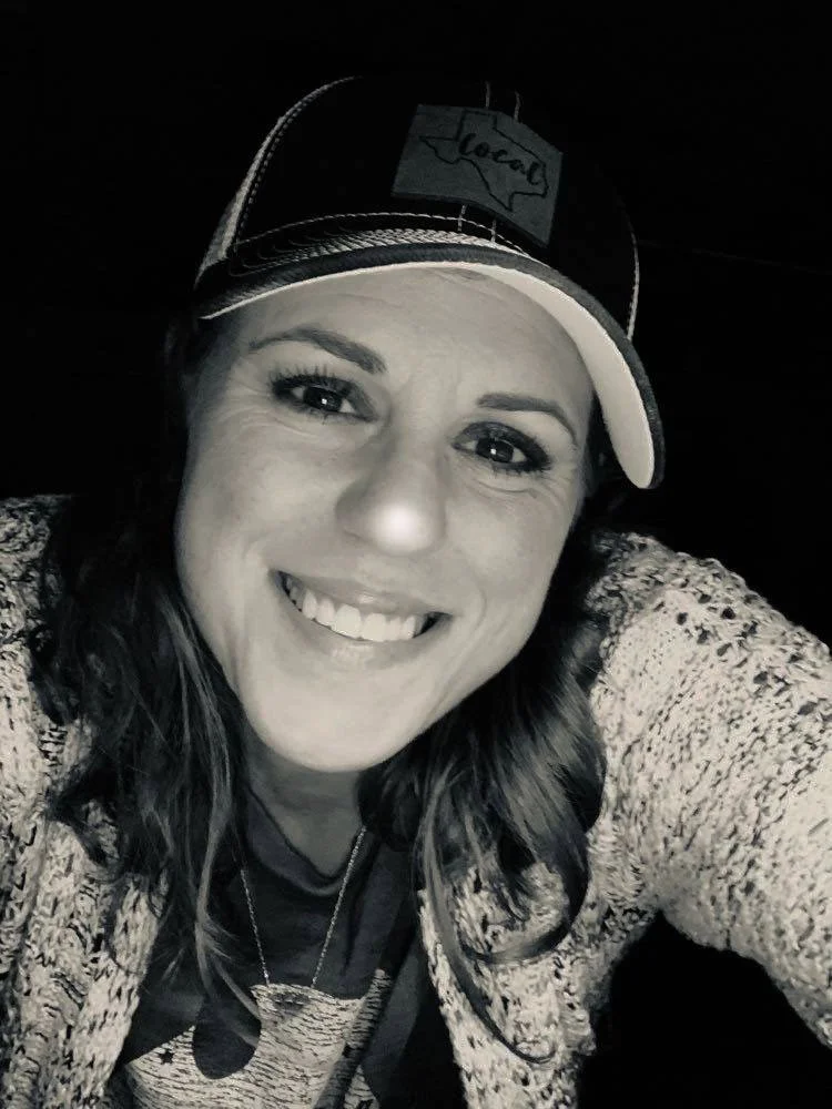 A woman smiling, wearing a baseball cap with the word "local" on it, and a patterned sweater.