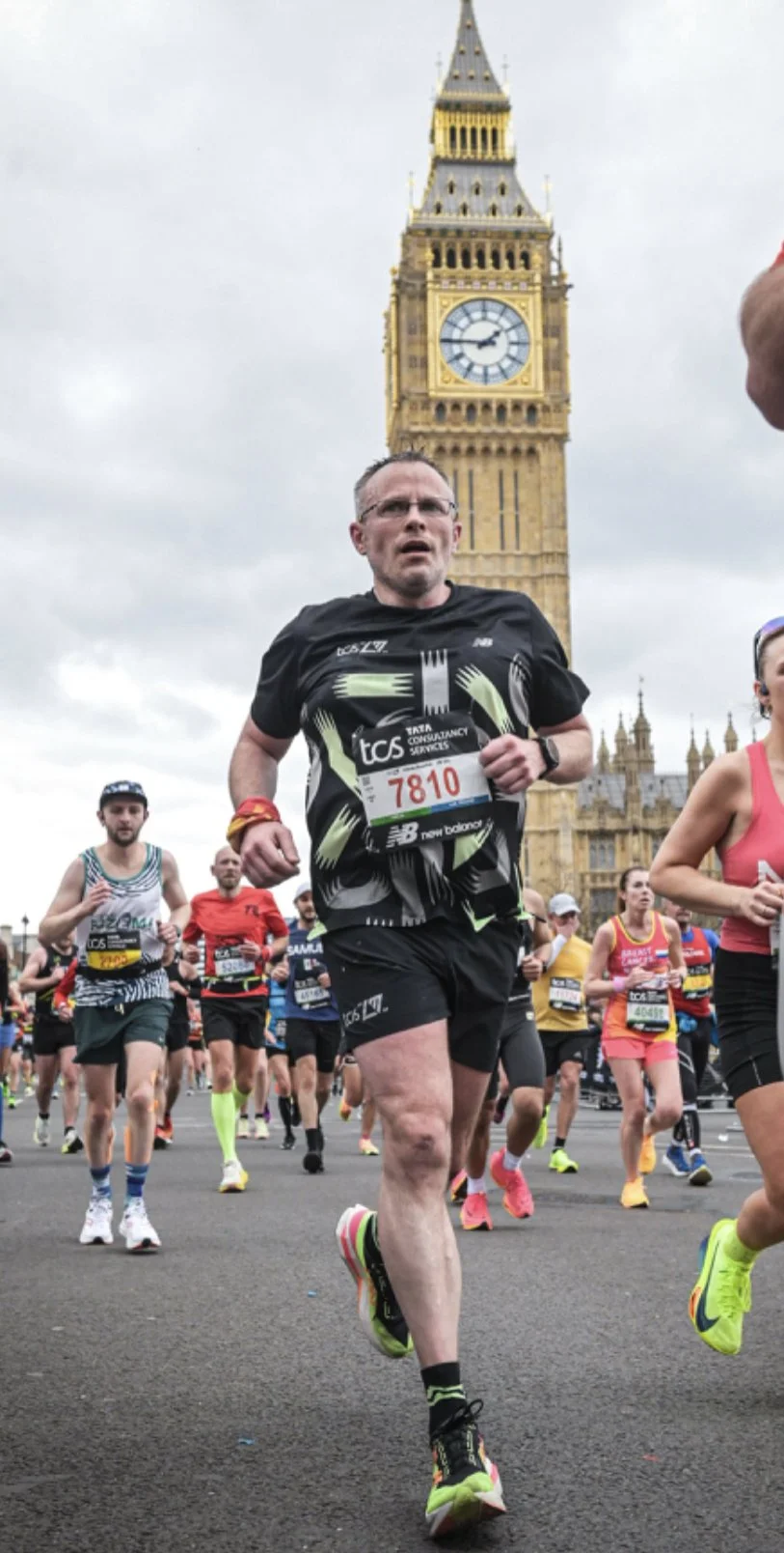 London Marathon runners participating in a race near Big Ben in London, with cloudy skies overhead.