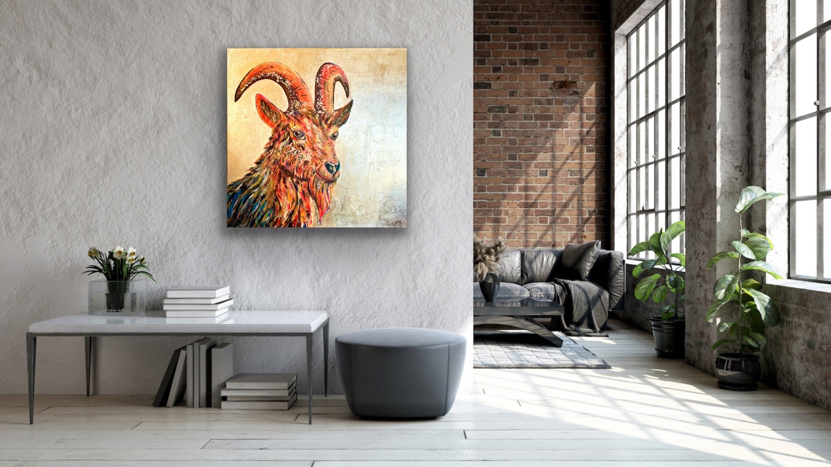 Interior of a modern loft with a white textured wall, a colorful painting of an antelope with curved horns, a white table with flowers and books, a gray ottoman, a gray leather sofa with pillows, potted plants, large windows, exposed brick wall, and 