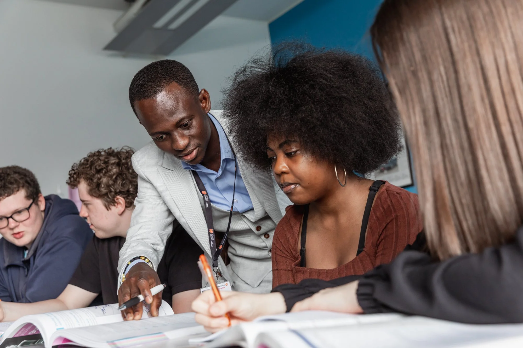 A teacher assists students with their work at a desk in a classroom.