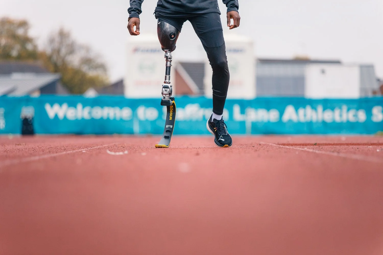 A person with a prosthetic leg running on a track at an athletic stadium.
