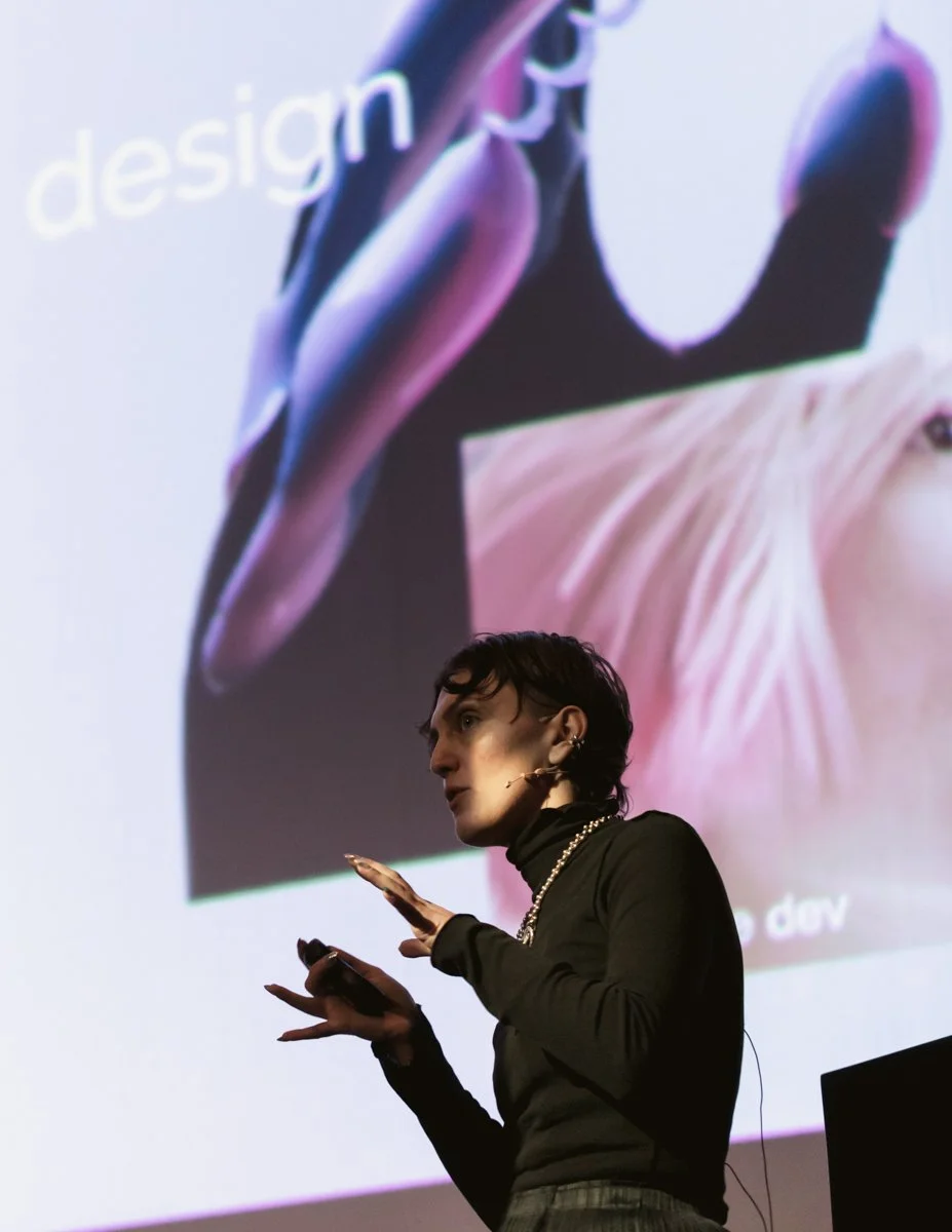 A woman giving a presentation in front of a large projected slide with the word 'design' visible.