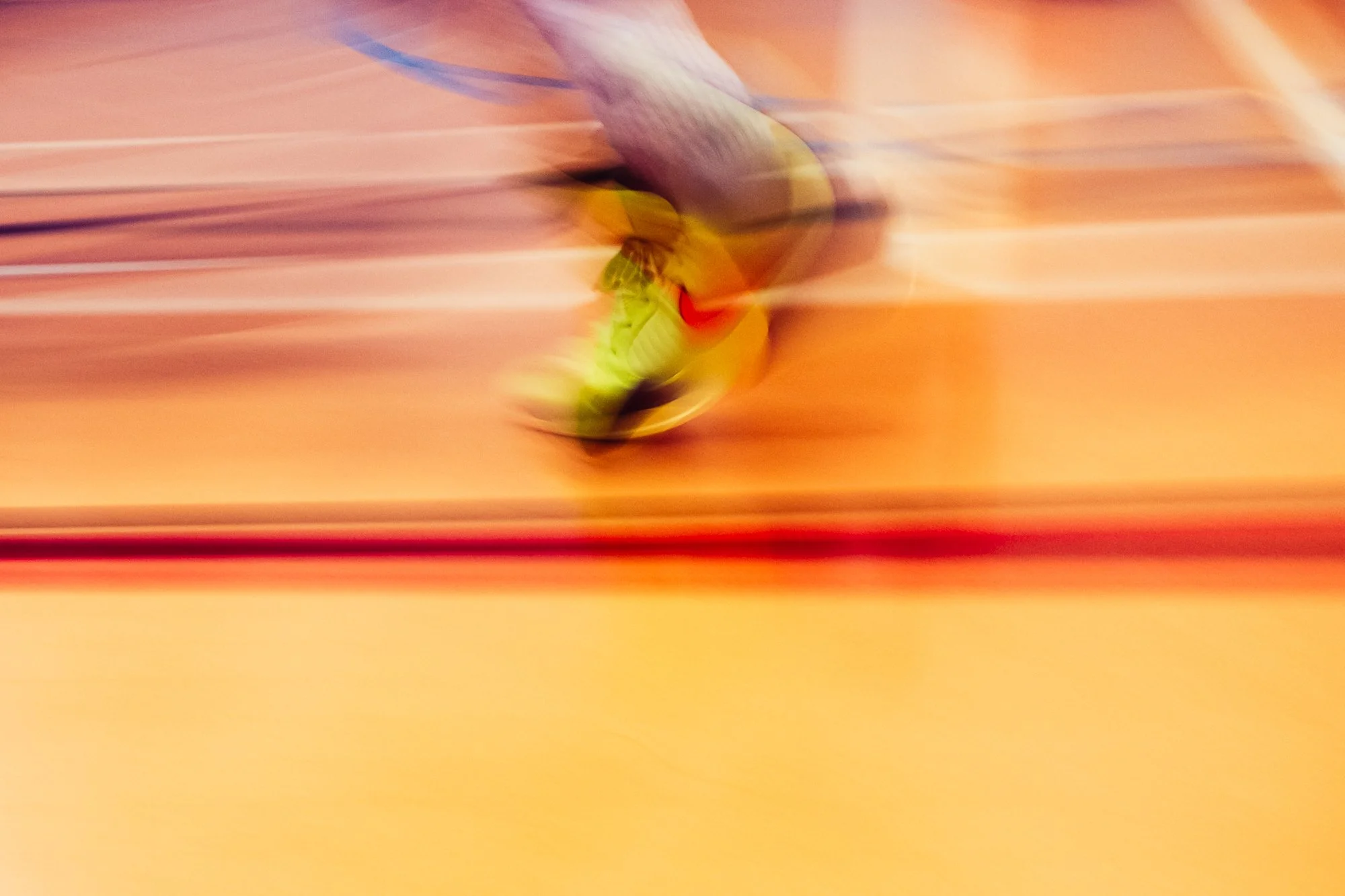 Blurred image of a person running on an indoor track, with streaks of orange and red background.