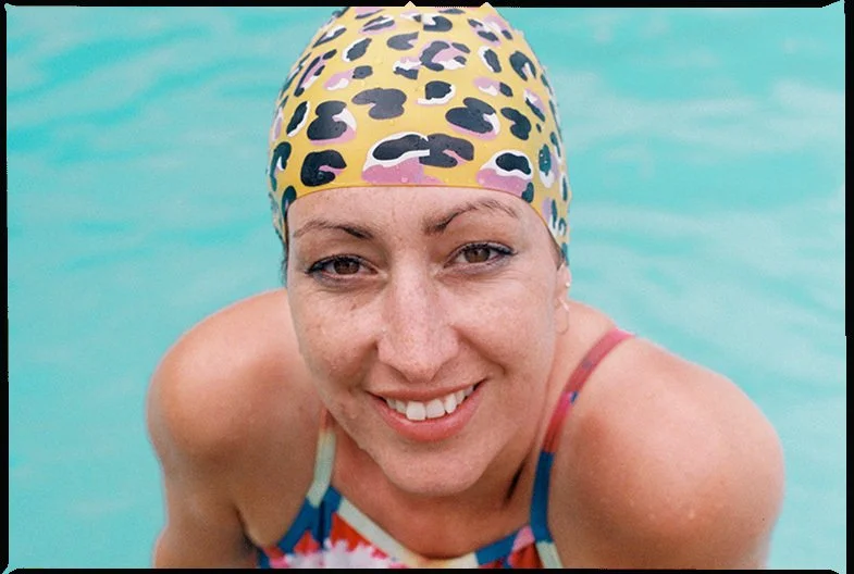 Close-up of a smiling woman in a swimming pool wearing a colorful patterned swim cap.