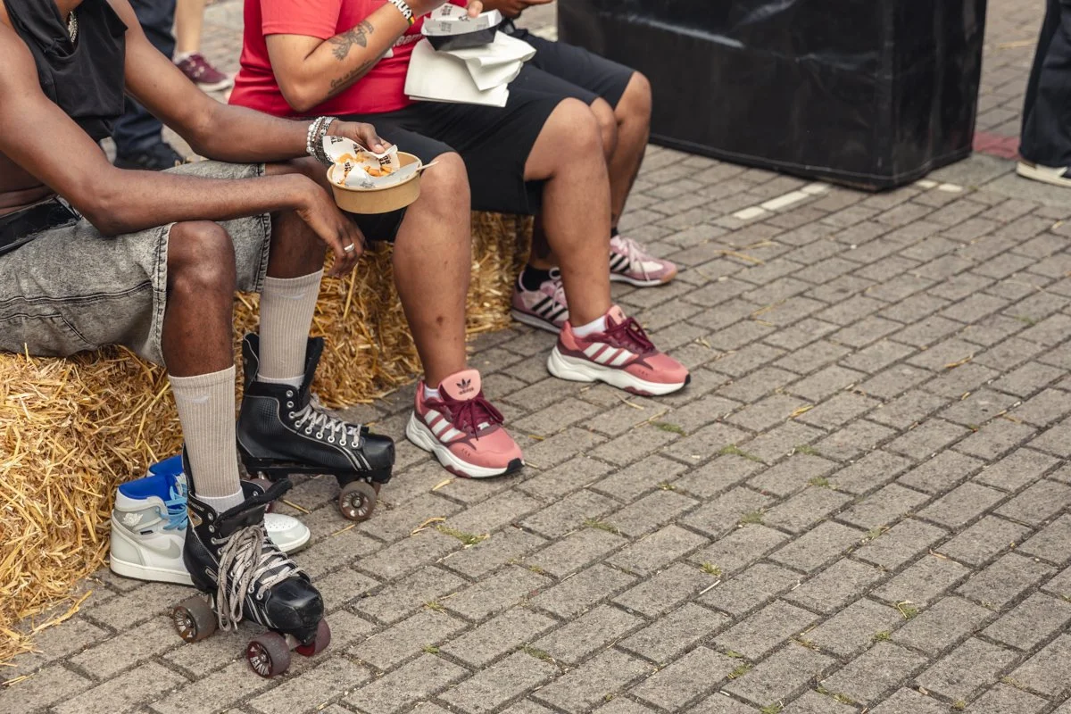 People sitting on hay bales, wearing roller skates and sneakers on a brick pavement