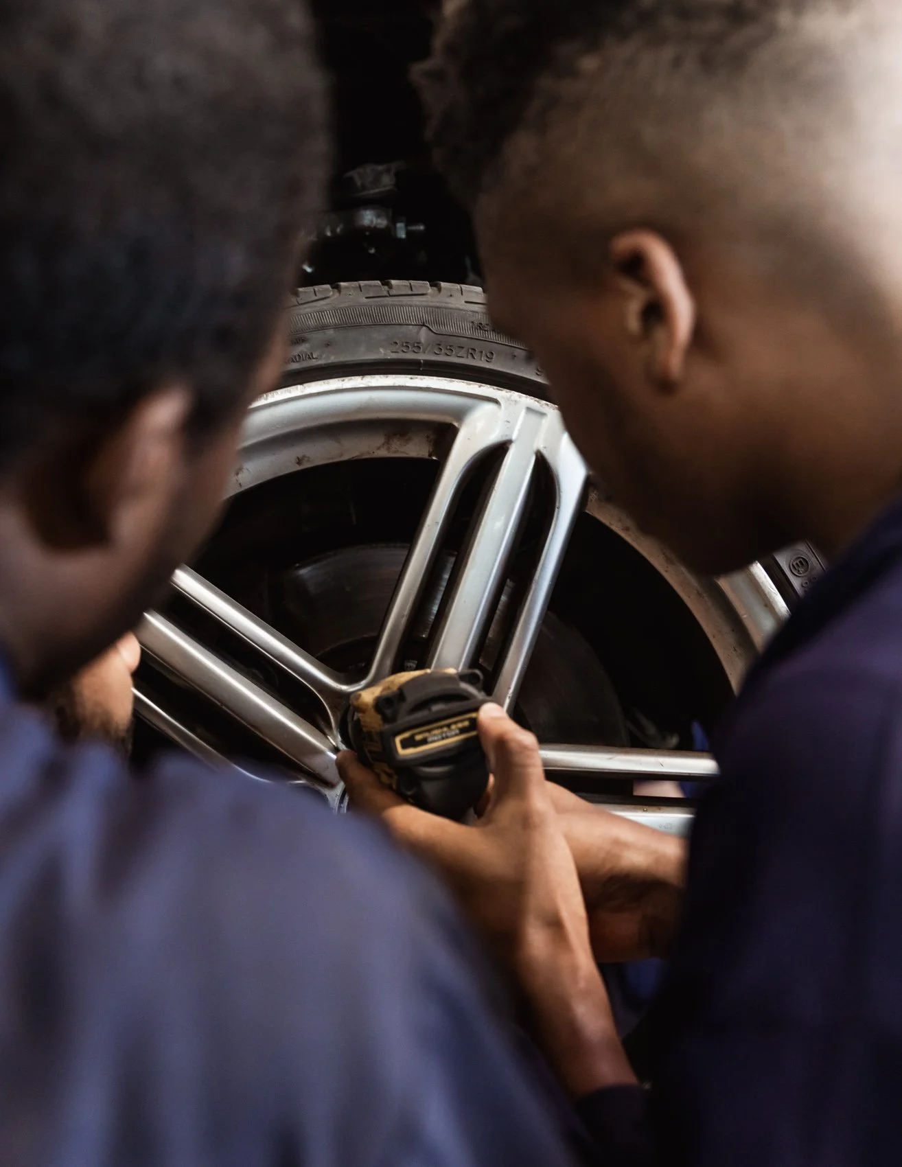Two people working on changing or repairing a car wheel using a power tool.
