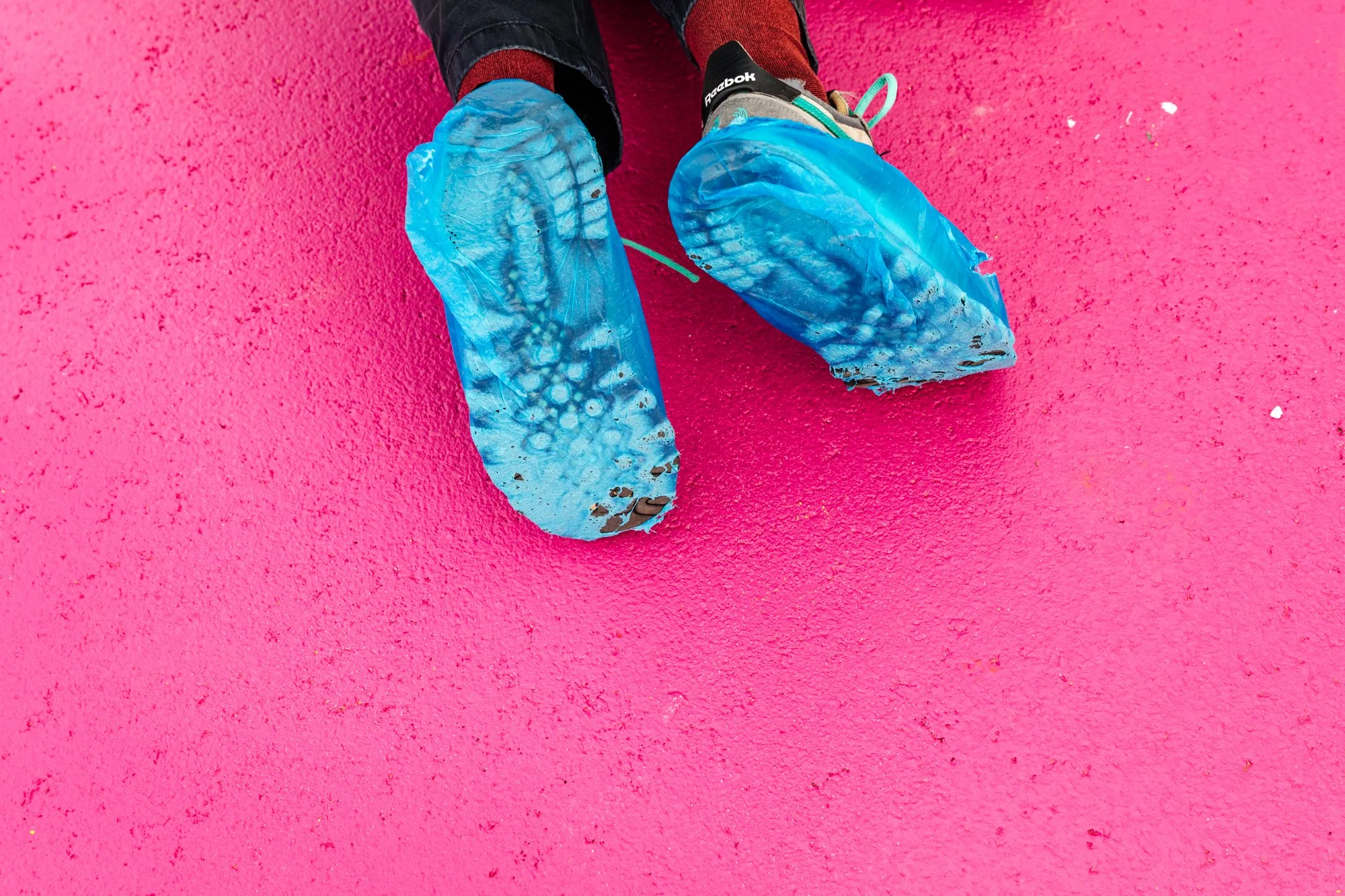Person wearing blue shoe covers sitting on a pink textured surface.