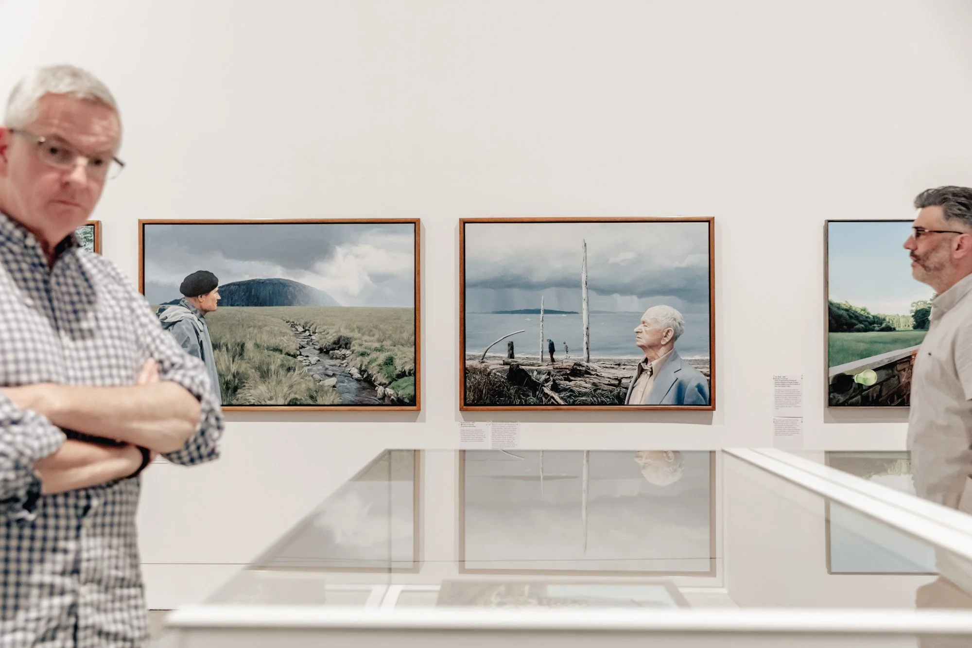 Two men in an art gallery looking at landscape photographs on the wall.