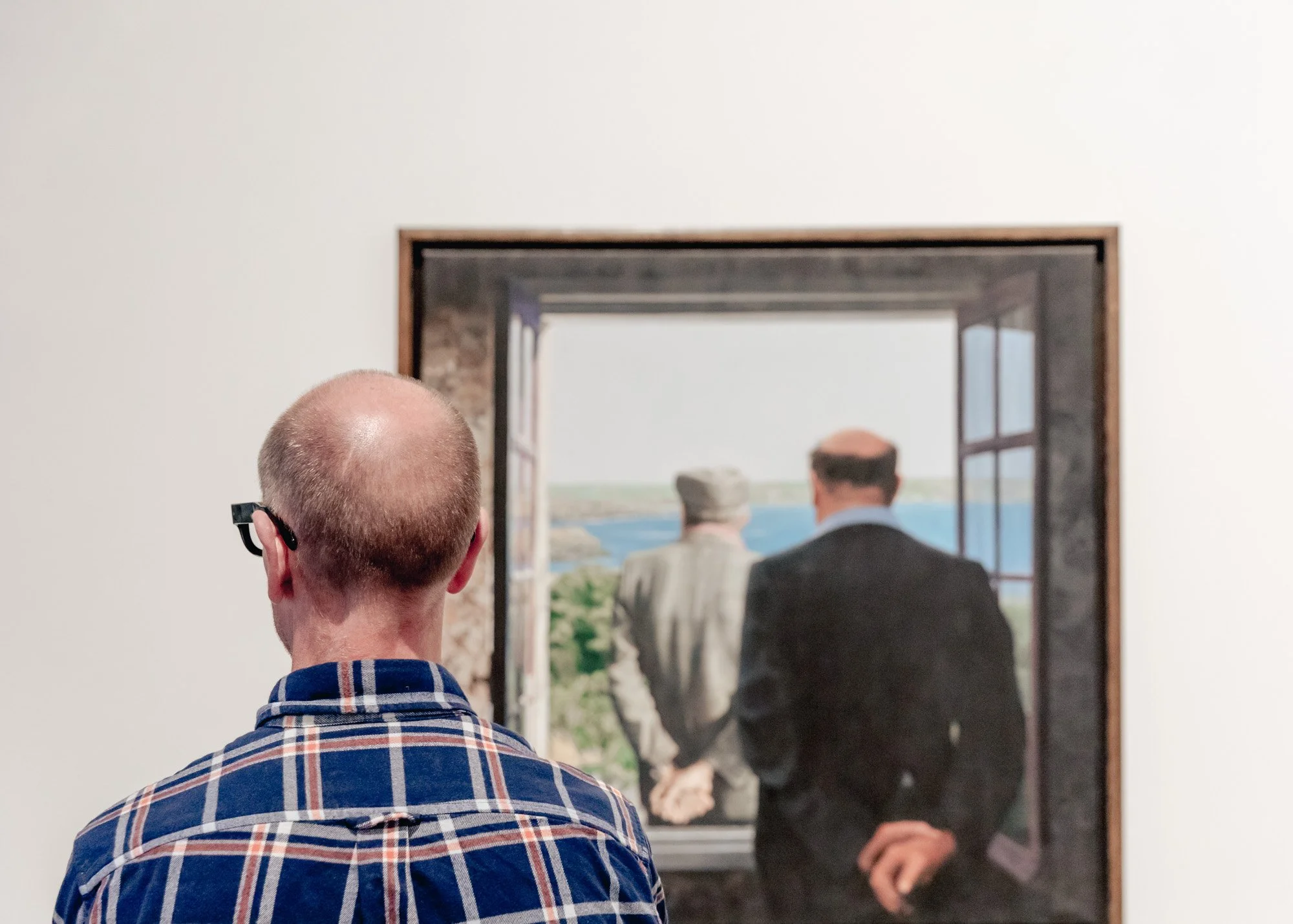 Person viewing a painting of two men standing by an open window overlooking water