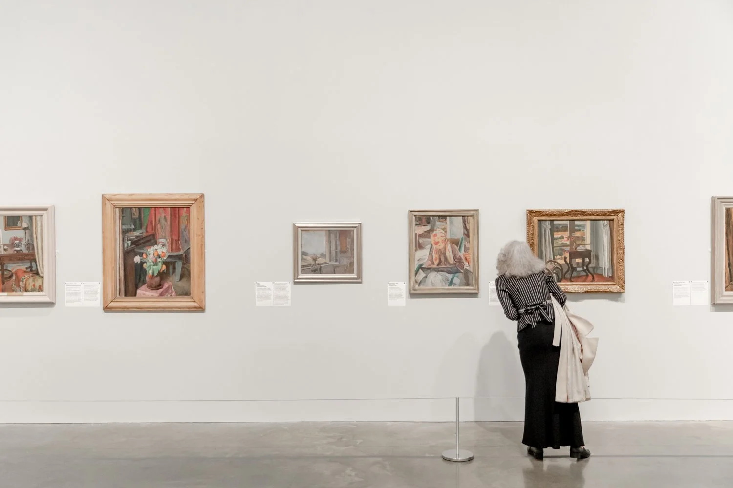 A woman with white hair looking at paintings in an art gallery.