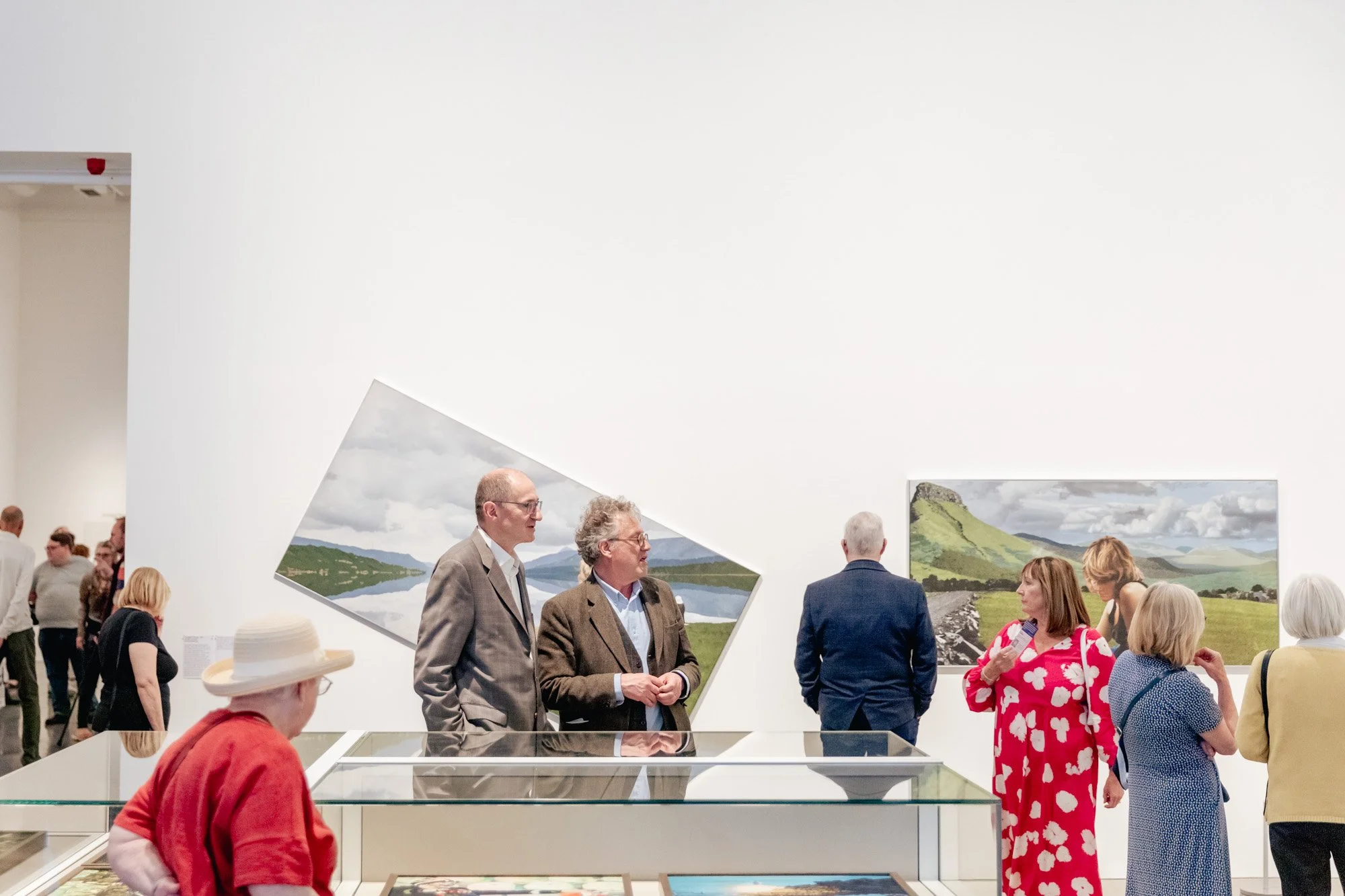Gallery visitors observing landscape paintings on display in an art museum.