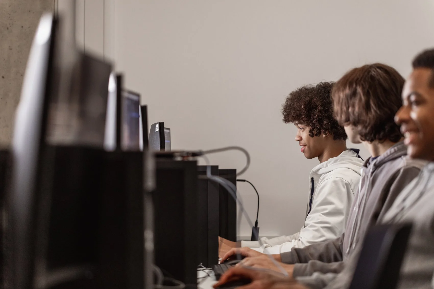 Three young people using computers in a row in a computer lab or class.