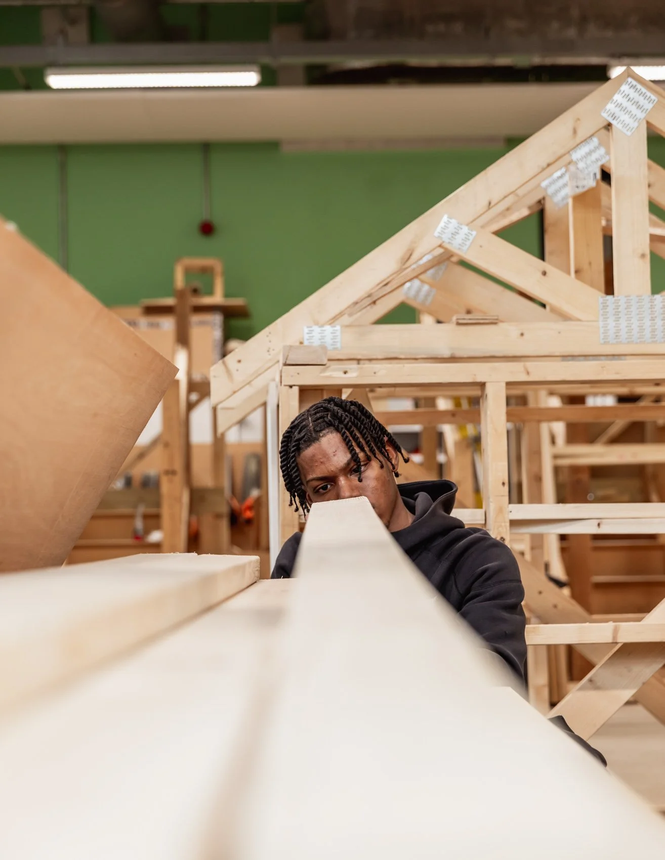 A man with dreadlocks inspecting wooden furniture frames in a woodworking shop.
