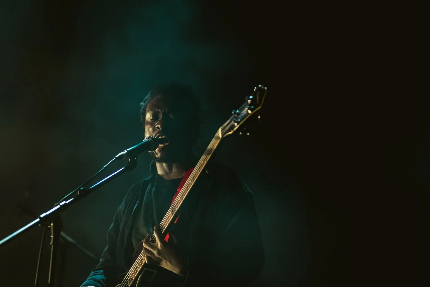 A man singing into a microphone and playing an electric guitar on a dark stage.