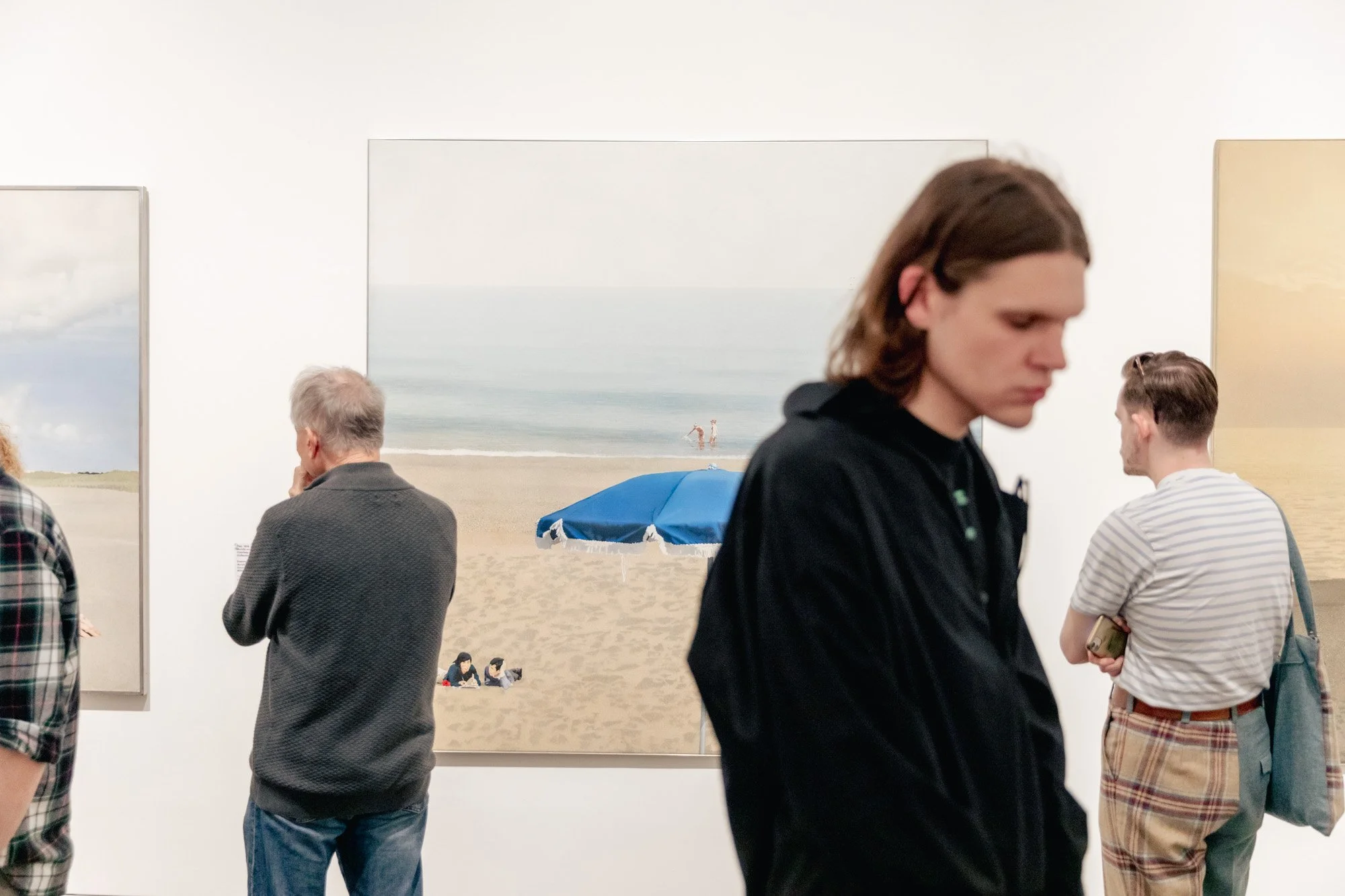 People viewing beach landscape photographs at an art gallery.
