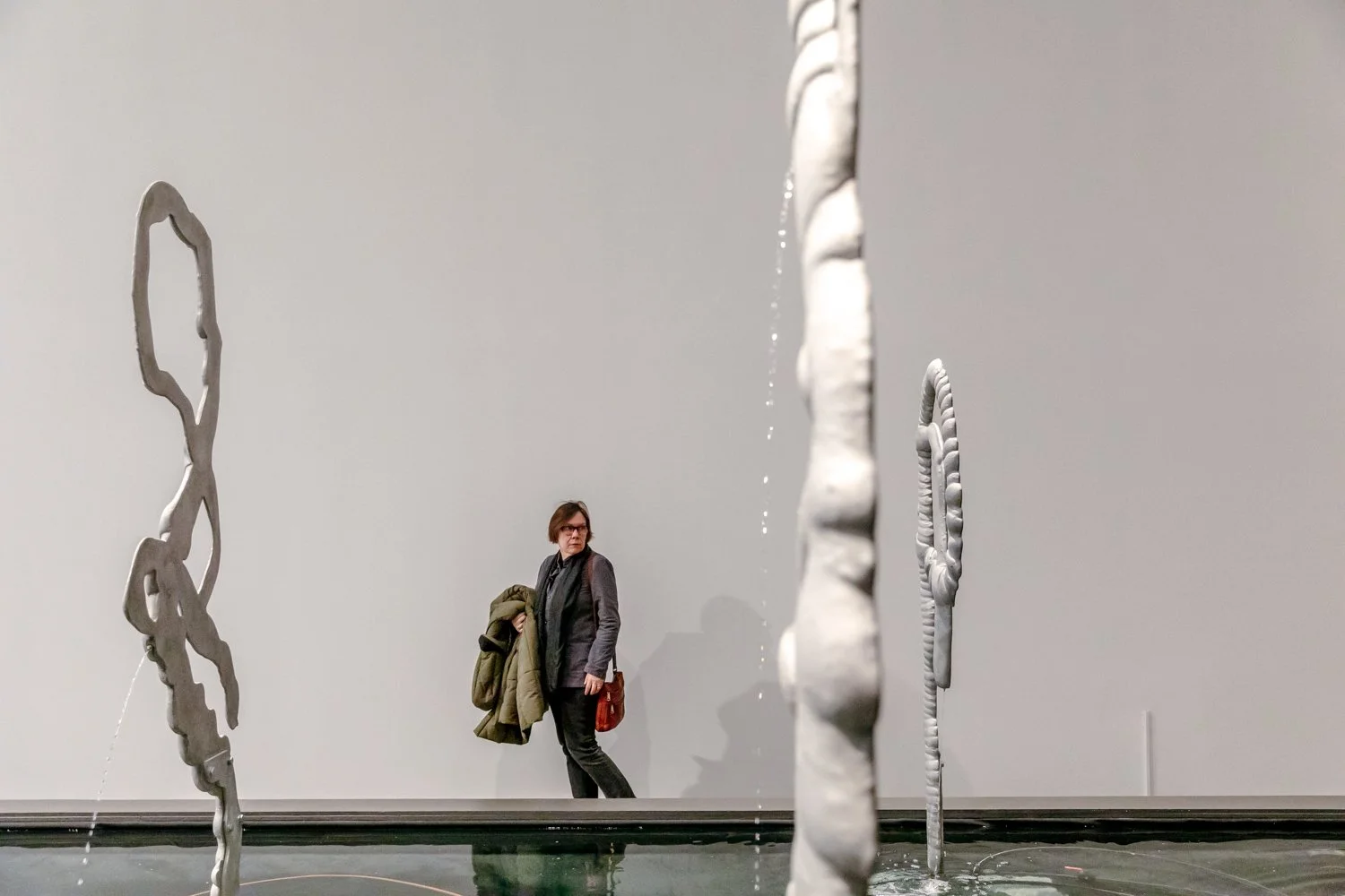 A woman standing near modern water fountains in an art gallery or museum.